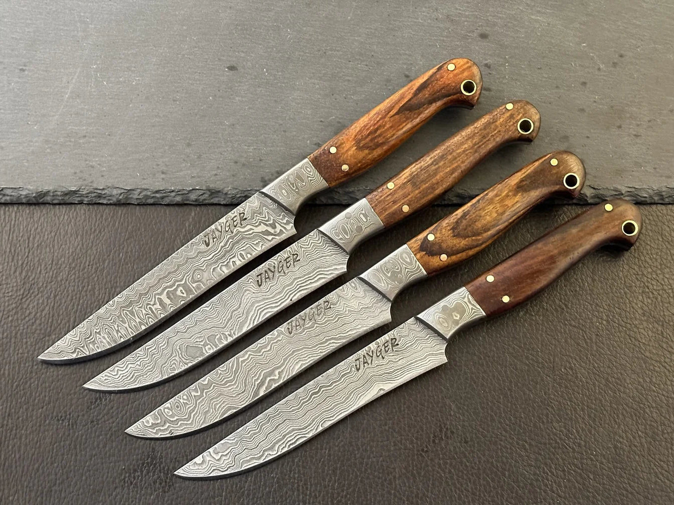 Set of four Damascus steel knives with wooden handles on a dark surface